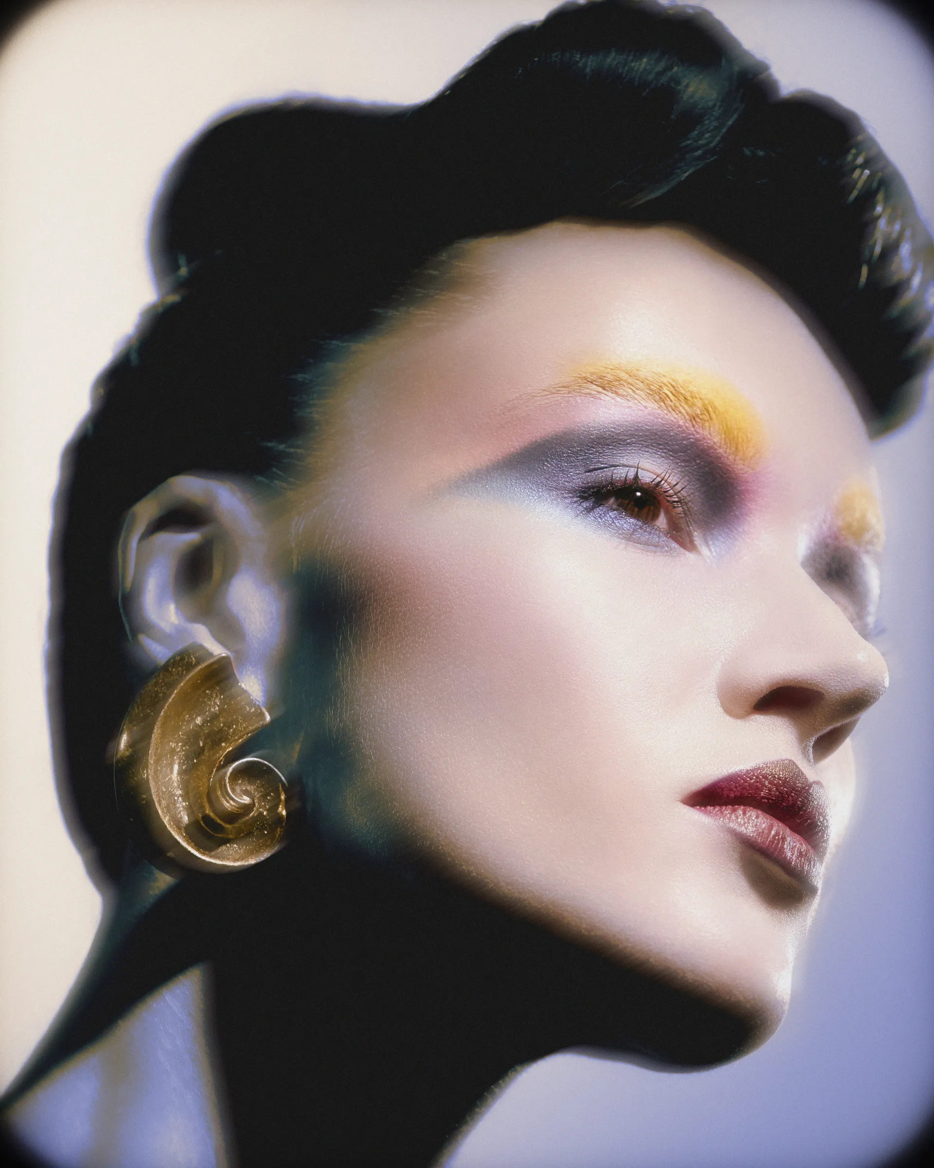 Beauty portrait with yellow and blue graphic eye makeup and a gold swirl earring