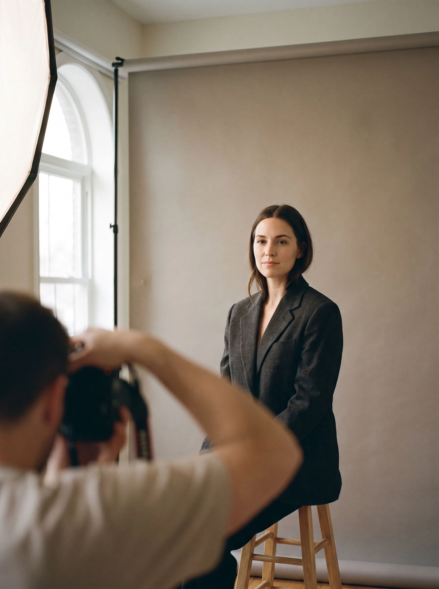 A woman in a charcoal blazer seated for a portrait against a grey backdrop
