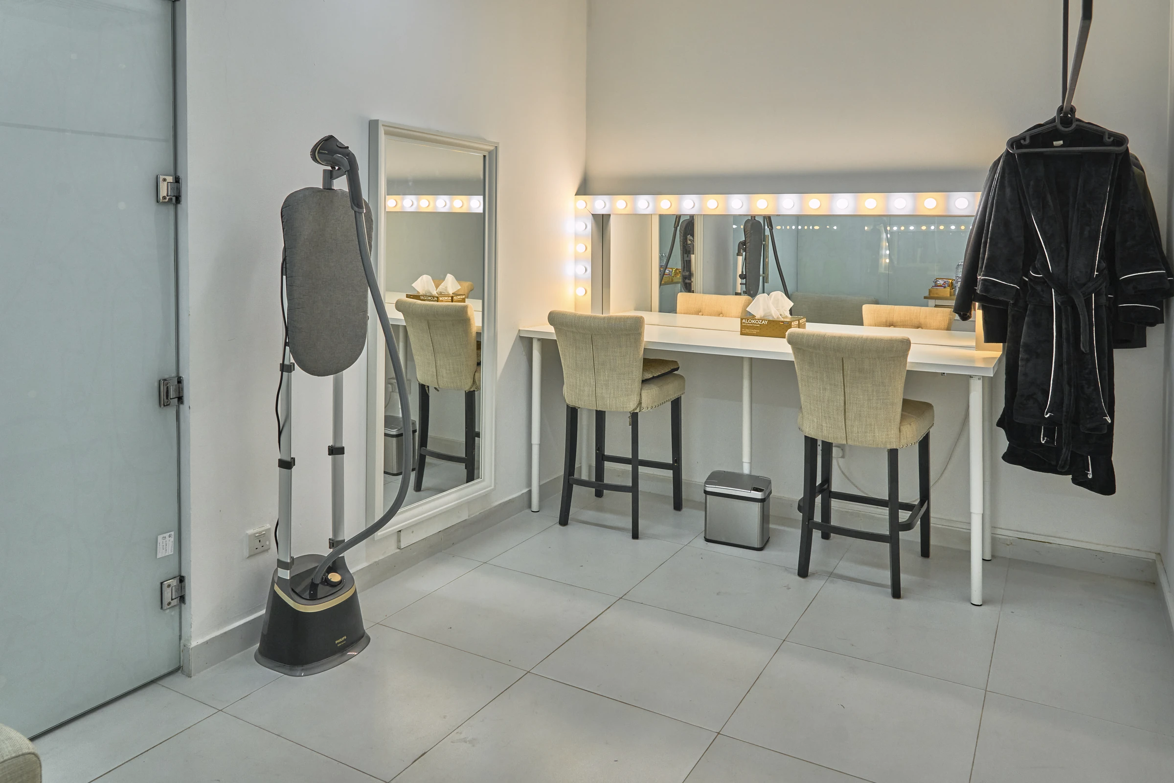 The hair and makeup room with a lit mirror, stools, a rail and a steamer